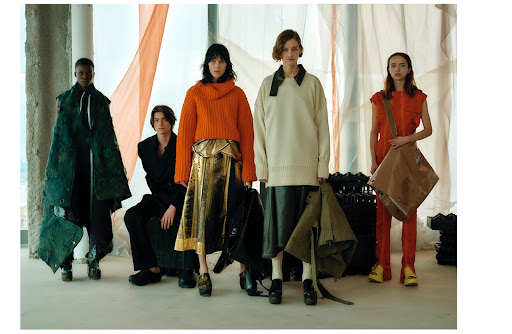 Five fashion models in unique clothing pose indoors with natural light and neutral backgrounds, showcasing distinctive textures and modern design.