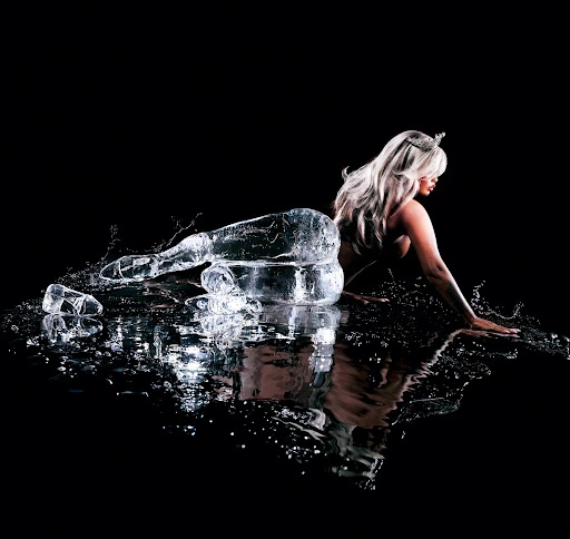 Woman posing as a mermaid with an ice tail and water droplets in a studio with a black background and dramatic lighting.