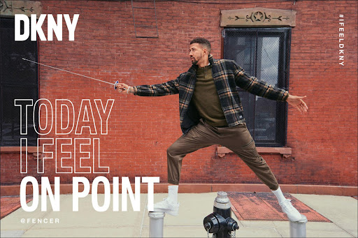 A man in stylish casual wear balances on metal posts with a fencing sword against a brick wall in an urban fashion advertisement for DKNY.