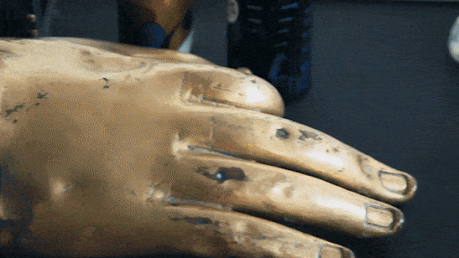 Close-up of a golden hand sculpture with textured details, showcasing artistry and craftsmanship on a dark surface.