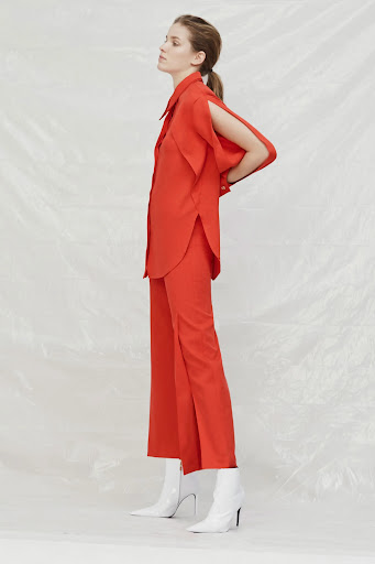 Studio shot of a fashion model posing in an orange two-piece suit with a button-down shirt, wide-leg pants, and white heeled boots.
