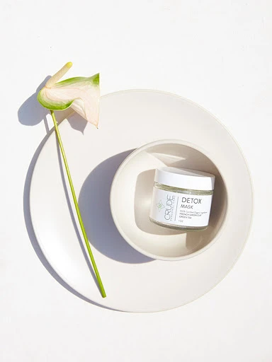 Product shot of a jar of detox mask on a white plate with a calla lily. Perfect for skincare, beauty, or spa concepts.