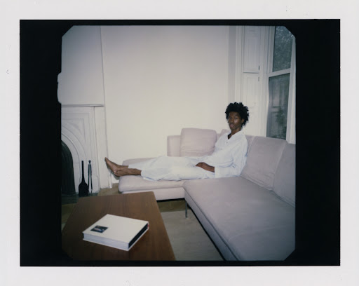 Woman lounges on a pink sofa in a bright, minimal living room. A coffee table sits in front of the couch in this eye-level shot.