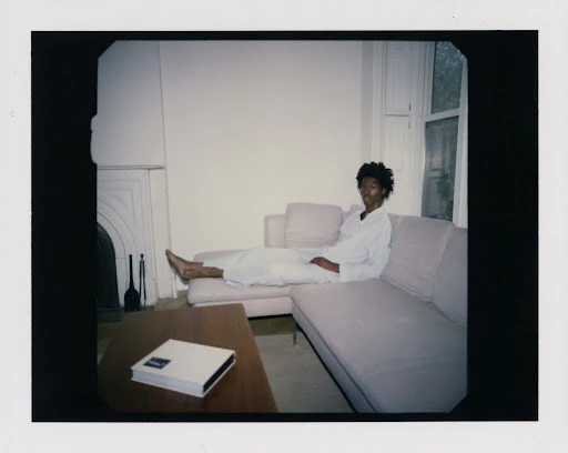 Woman lounges on a pink sofa in a bright, minimal living room. A coffee table sits in front of the couch in this eye-level shot.
