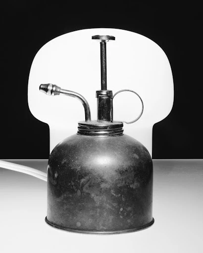 Close-up studio shot of a metal oil can with a pump nozzle, against a split black and white background and white surface.
