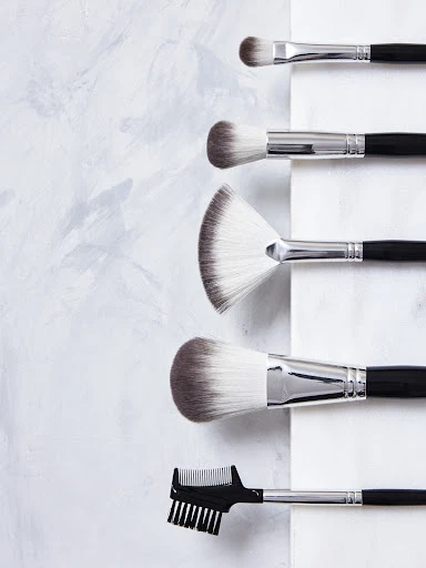Overhead shot of black-handled makeup brush set arranged vertically on a white and grey marble surface, beauty and cosmetics concept.