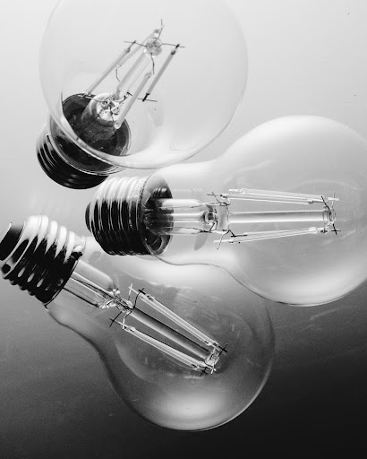 Three light bulbs are shown in a black and white studio shot, featuring clear glass and visible filaments, creating an abstract still life.