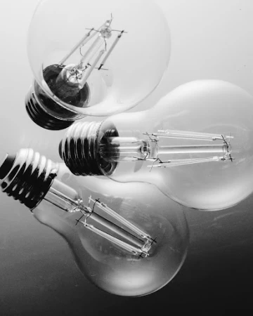 Three light bulbs are shown in a black and white studio shot, featuring clear glass and visible filaments, creating an abstract still life.