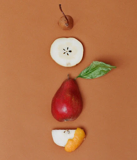 Still life of sliced and whole pears in a vertical composition on a brown background, emphasizing culinary art and food photography.