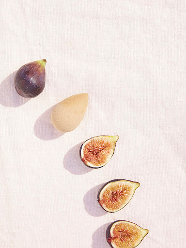 Overhead shot of a halved figs and a makeup sponge on a white textured fabric background. Food photography, beauty product image.
