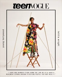 Letitia Wright standing on a wooden folding chair holding wooden poles against a white studio background, styled by Kate Stein.