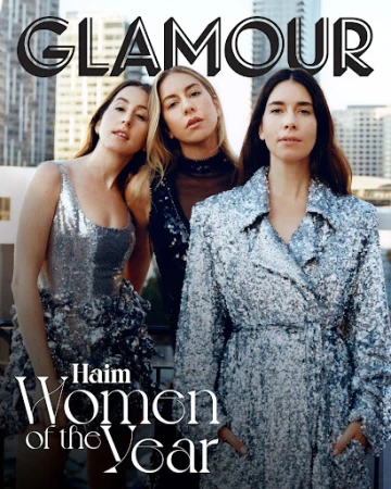 Glamour magazine cover featuring the Haim sisters in sparkly dresses and coats, standing against a city skyline backdrop.