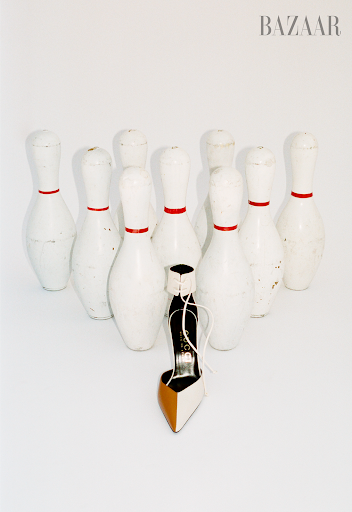 Fashion still life: A high-heeled shoe placed among bowling pins on a white background, creating a playful and stylish visual statement.