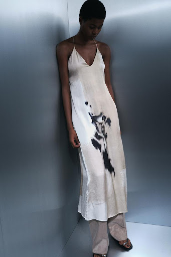 Model wearing a printed cream slip dress leaning against a metallic grey studio wall by set designer Kelly Infield.
