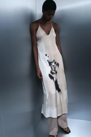 Model wearing a printed cream slip dress leaning against a metallic grey studio wall by set designer Kelly Infield.