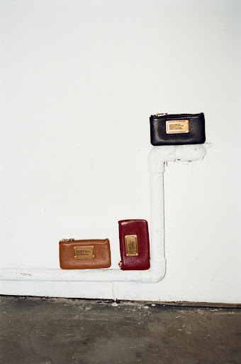 Three leather wallets are arranged in a vertical line on a white pipe against a stark white wall, offering a minimalist aesthetic.