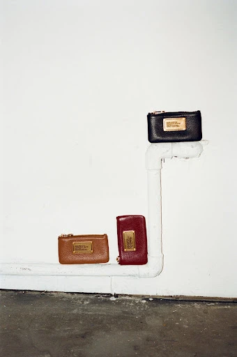 Three leather wallets are arranged in a vertical line on a white pipe against a stark white wall, offering a minimalist aesthetic.
