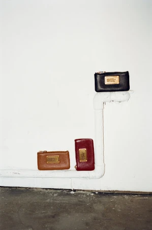 Three leather wallets are arranged in a vertical line on a white pipe against a stark white wall, offering a minimalist aesthetic.