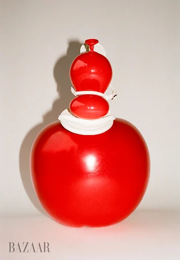 Red glass sculpture with a round base and stacked spherical shapes against a white background, illuminated by studio lighting.