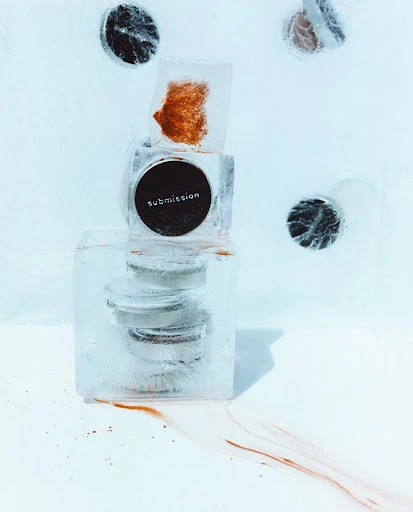 A stack of cosmetics encased in clear ice blocks, set against a bright white background, highlighting beauty and frozen aesthetics.
