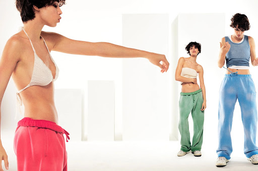 Three slender young women model knit bikini tops and sweatpants in a minimalist studio with white blocks in the background.