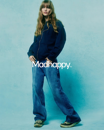 A young adult woman in jeans and a hoodie poses in a studio with a light blue background. Fashion shot. Full body view. Studio lighting.