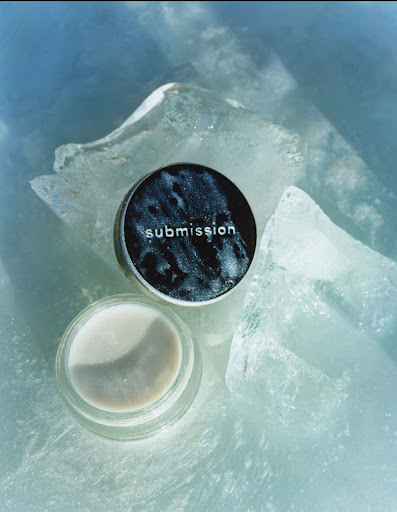 Two skincare containers, one open and one closed, rest on a textured, translucent blue and white surface resembling ice.
