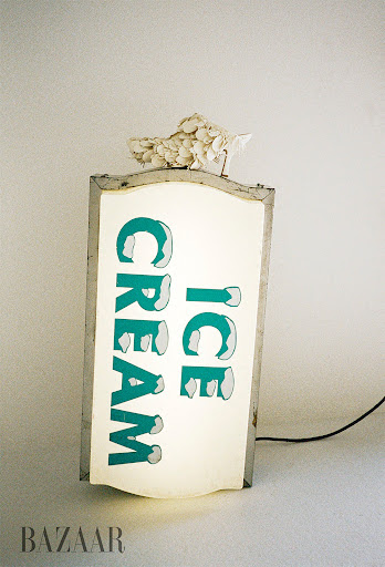 Illuminated vintage Ice Cream sign with white floral decoration, glowing against a neutral background. Retro, nostalgic.