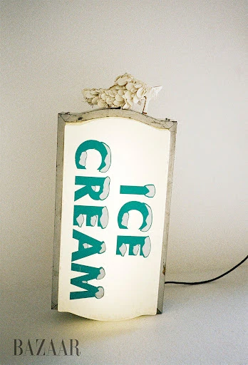 Illuminated vintage Ice Cream sign with white floral decoration, glowing against a neutral background. Retro, nostalgic.