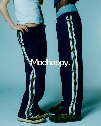 Two figures display navy sweatpants with white crochet stripes, paired with sneakers, against a cool blue studio backdrop. Madhappy logo.