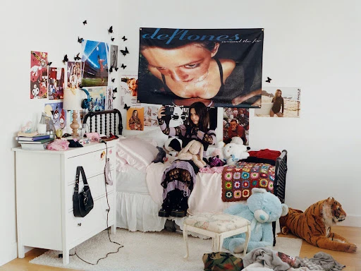 Teenager in bedroom with Deftones banner. The room features posters, a bed with stuffed animals, and personal belongings creating a personalized space.