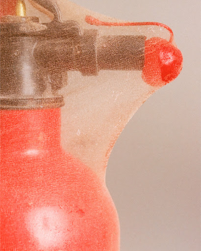 Close-up of a red fire extinguisher wrapped tightly in sheer translucent fabric with a red cherry shape attached.