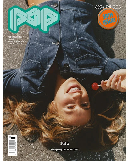 Magazine cover featuring a woman in a denim jacket lying on a concrete surface, holding a lollipop, with the 'POP' logo displayed prominently.