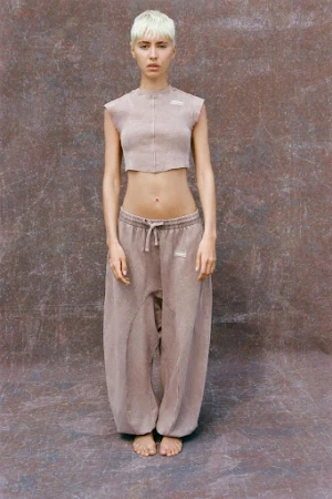 Model with short platinum blonde hair wearing a cropped top and loose trousers against a textured mottled backdrop