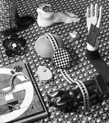 Black and white still life featuring mannequins, jewelry, and various props on a patterned surface, creating an elegant and artistic display.
