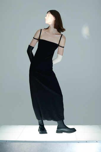 Adult female fashion model in a black slip dress and black leather boots poses in a studio with mixed black and white gloves.