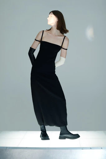 Adult female fashion model in a black slip dress and black leather boots poses in a studio with mixed black and white gloves.