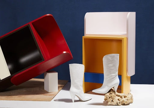 Fashion shot featuring white heeled boots with a pointed toe, styled with colourful architectural furniture in a studio setting.