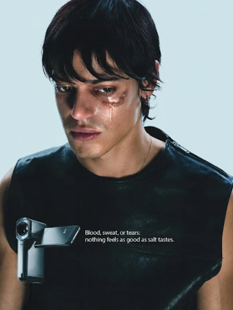 Close-up of a young man with tears on his face, wearing a dark sleeveless shirt, with a video camera attached to the shirt.