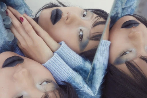 Artistic portrait featuring a reflective surface and an Asian woman with striking dark lipstick and pale eyeshadow, wearing a light blue sweater.