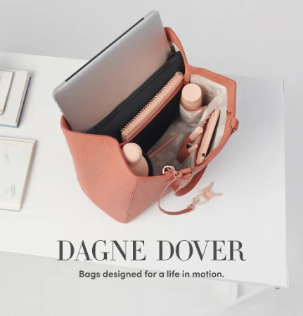 Salmon-colored Dagne Dover tote bag on a white surface, open to reveal a laptop, journal, cosmetics, and other personal items inside.