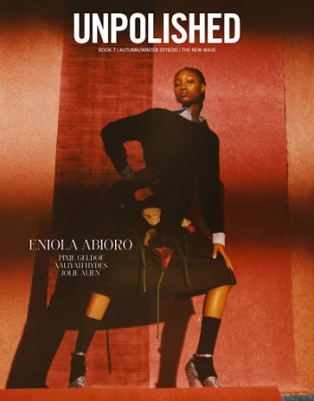 Fashion magazine cover featuring a Black woman in a dark outfit and glittery heeled boots, posing in front of an orange backdrop.