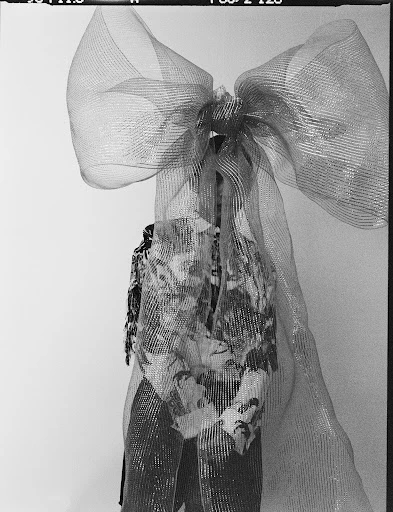 Abstract fashion shot of a patterned top and pants ensemble with a large sheer bow against a white background in a studio setting.