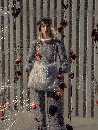 Fashion shot of woman in knit pantsuit with a furry apron and matching beret, posing in front of white fence with flowers. 