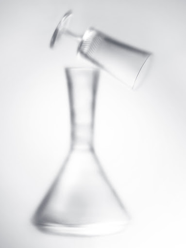 A clear carafe and angled glass create a visually striking composition against a clean, bright background, blending form and simplicity.