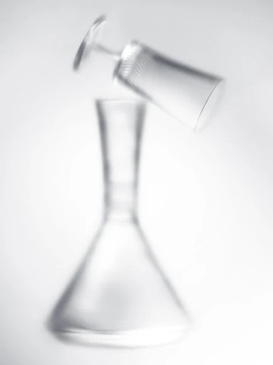 A clear carafe and angled glass create a visually striking composition against a clean, bright background, blending form and simplicity.