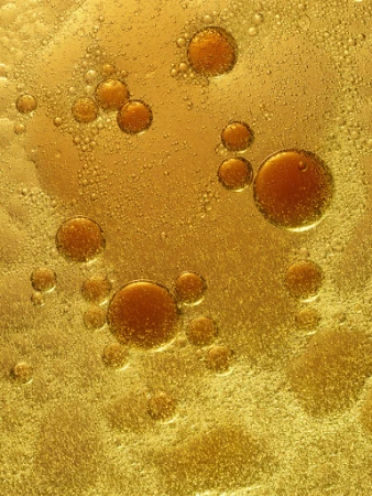 Macro view of golden oil droplets floating on liquid surface with amber bubbles and shimmering textures.