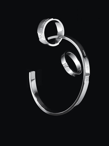Silver metallic rings and a curved cuff bracelet floating against a plain dark black background.