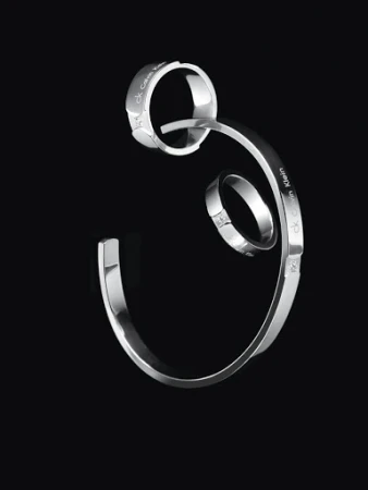 Silver metallic rings and a curved cuff bracelet floating against a plain dark black background.
