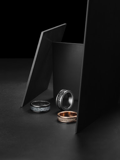Three rings are arranged with geometric shapes creating a sophisticated jewelry product shot on a sleek black surface.